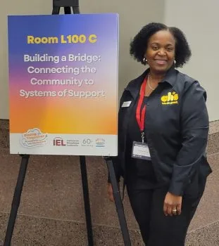 A woman stands beside a sign indicating Room L100C