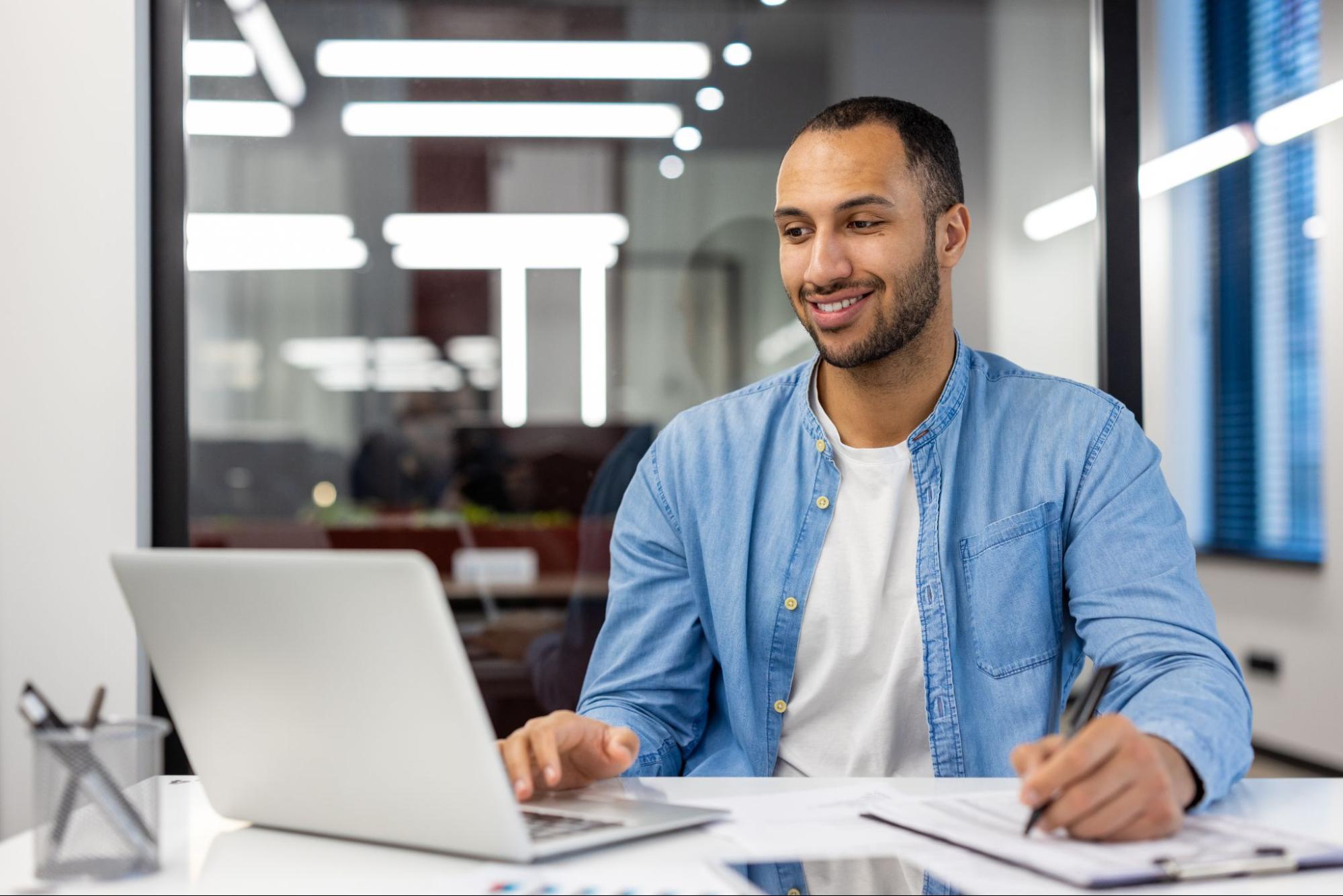 A male online student sits at his desk and takes notes during his online education courses