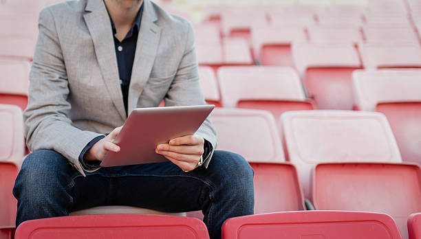 Professional Sports Careers: Sports Event Manager A sports manager sitting in stadium seats with a tablet, overseeing event operations and planning.