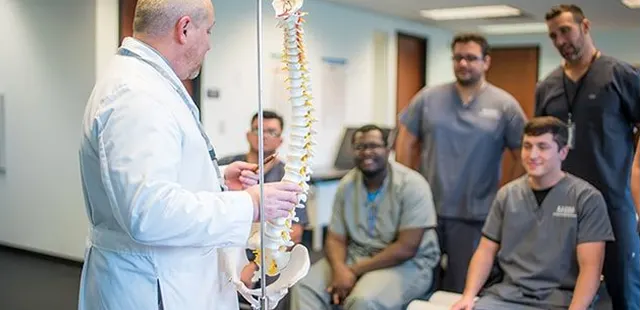 A group of people gathered in a room, with a large spine sculpture prominently displayed in the center.