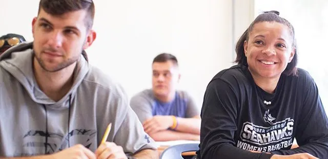 Two students seated at a classroom table, engaged in listening to the lesson.