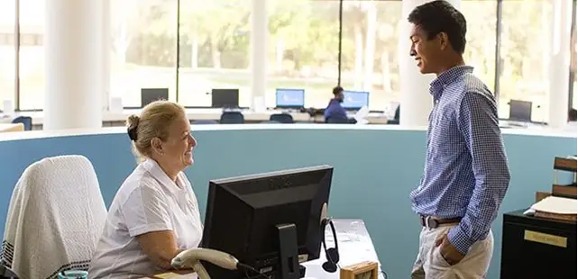A teacher and student engage in conversation while seated in front of a computer.