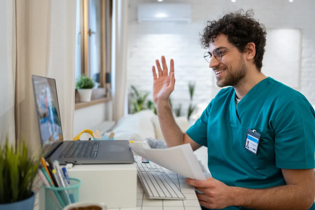 Male nurse in scrubs, waving back to a patient during a video call